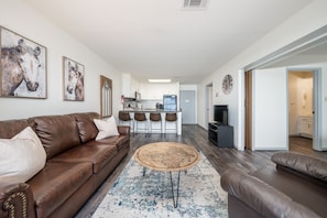 A modern living room with a brown leather sofa, a round coffee table, and a kitchen in the background.