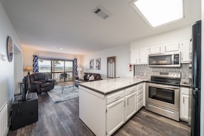 A modern kitchen with white cabinets, stainless steel appliances, and a large island. There is a dining area with a view of the outdoors.