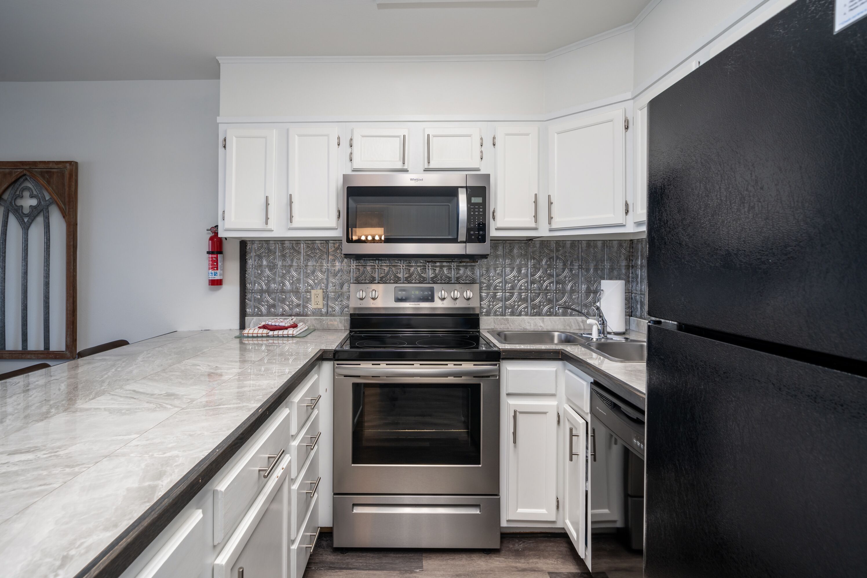 Una cocina moderna con armarios blancos, estufa de acero inoxidable, microondas y refrigerador negro.