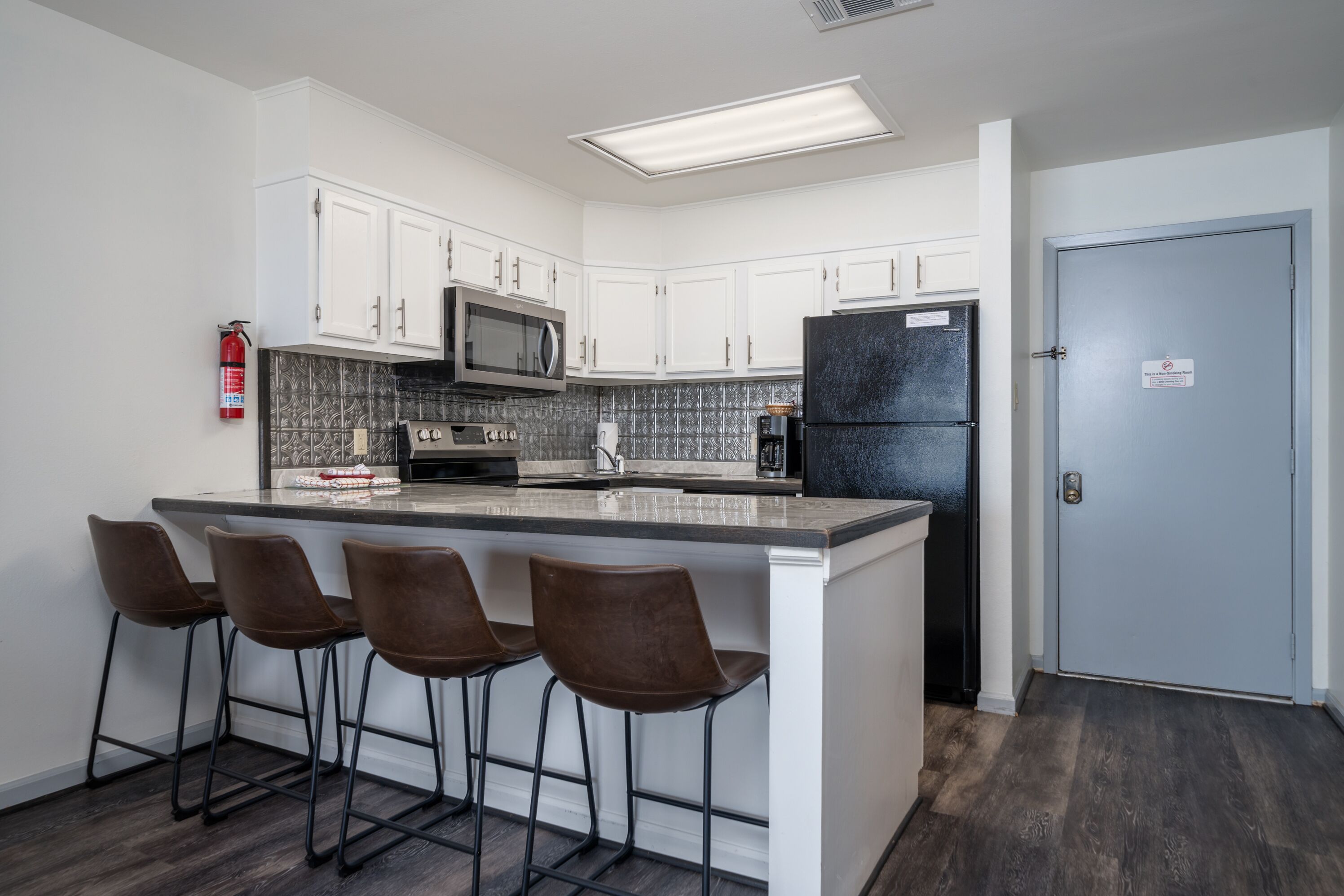 A modern kitchen with white cabinets, a black refrigerator, a microwave, and a bar area with stools.