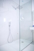 Une salle de bain moderne avec une douche à parois de verre, un lavabo blanc et des murs en marbre.