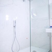 Una ducha con cerramiento de vidrio, grifo cromado y pared de mármol blanco.