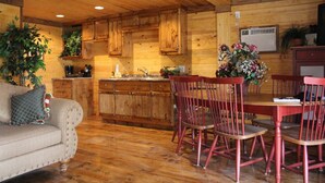 Um interior acolhedor em estilo cabana, com pisos de madeira, uma mesa de jantar com cadeiras vermelhas, um sofá com almofada estampada e armários de madeira.