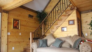 Um interior em madeira com escadas, um sofá com almofadas e decorações nas paredes.