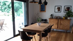 Een moderne eetruimte met een houten tafel en stoelen, een kast met decoratieve objecten en uitzicht door grote glazen deuren.