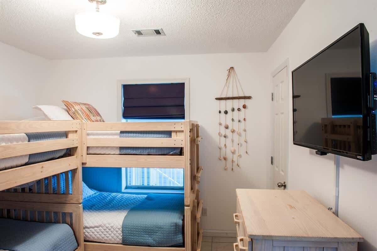 A room with bunk beds, a TV, a wall hanging, and a window.