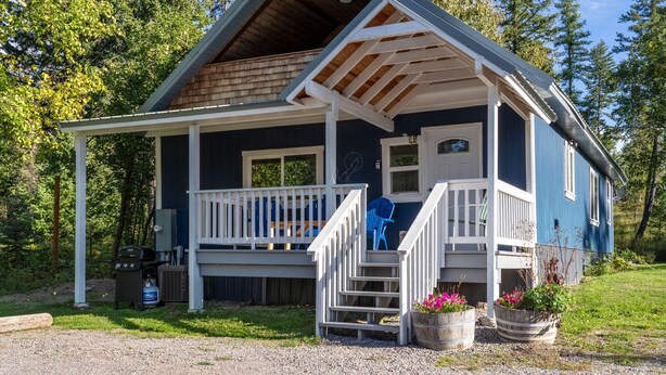 A two-story cabin with a porch, a staircase, and a grill outside.