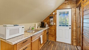 A compact kitchen with a microwave, sink, and wooden cabinets.