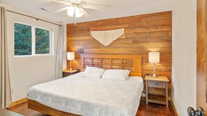 A bedroom with a wooden headboard, a bed with white linens, two bedside tables with lamps, and a ceiling fan.