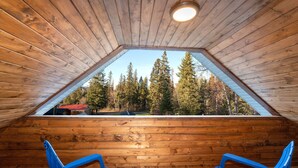 A wooden interior with a sloped ceiling and a view of a forest.