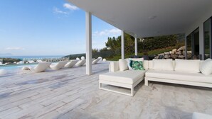 Un espace de détente extérieur moderne, doté d’une piscine, de mobilier blanc et offrant une vue sur la mer.