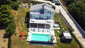 Une maison moderne à deux étages dotée d’une grande piscine, d’un espace extérieur aménagé et d’une cour clôturée.