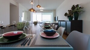 Un espace repas avec une longue table dressée pour un repas, plusieurs chaises et des lampes suspendues.