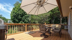 Une terrasse en bois avec une table et des chaises, un barbecue et un grand parasol.