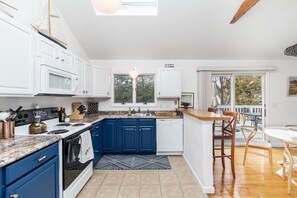 A modern kitchen with blue cabinets, white appliances, and a large window.
