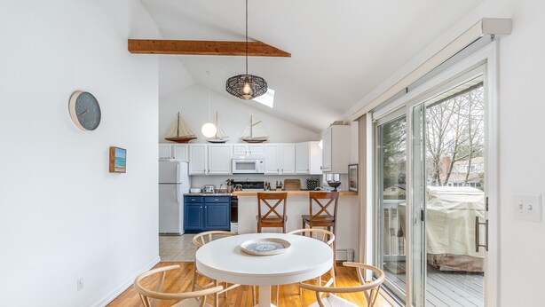 Une cuisine moderne avec des meubles blancs, un coin repas doté d’une table ronde et de chaises, et une grande porte-fenêtre coulissante donnant sur un espace extérieur.