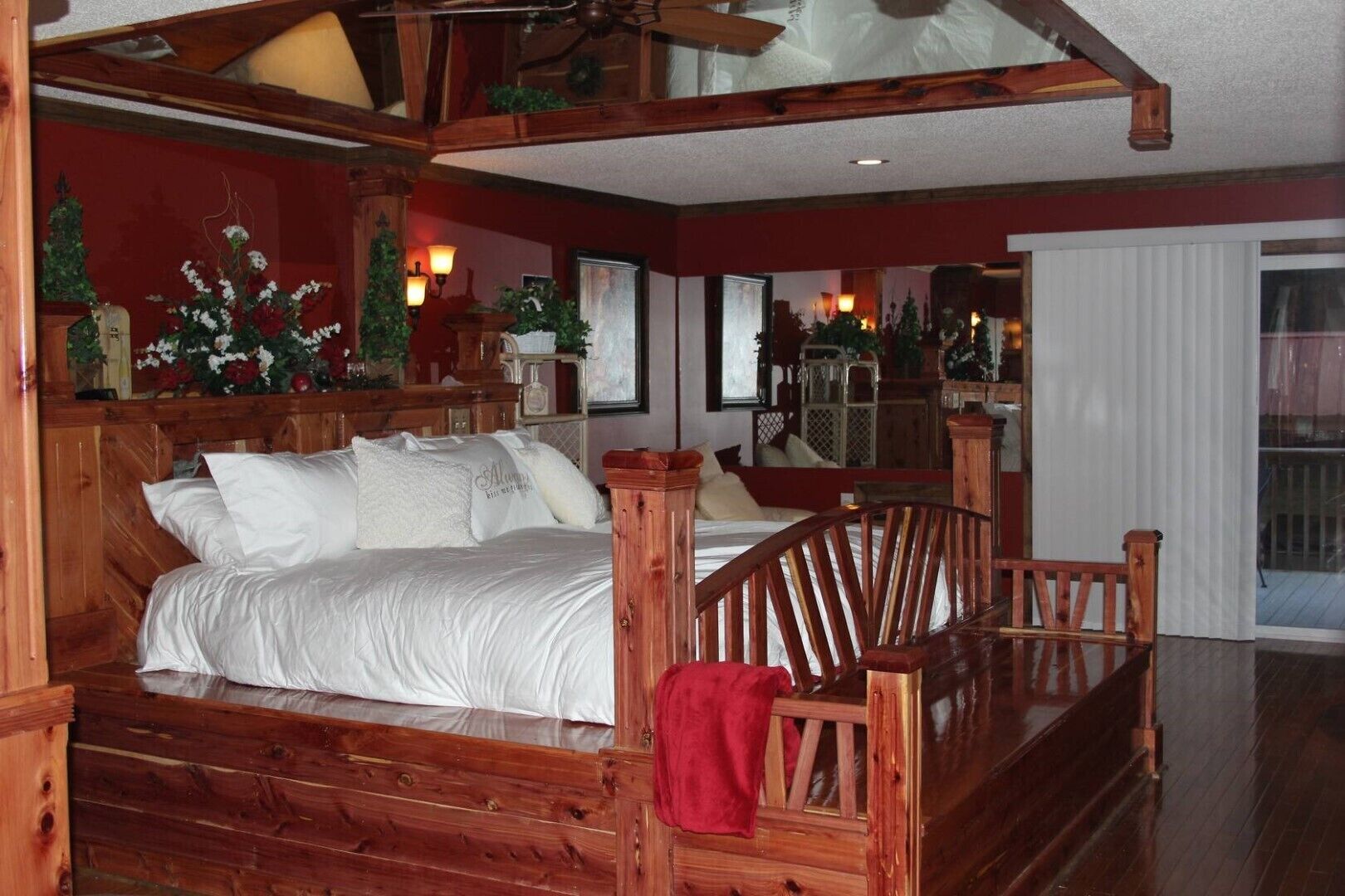 A wooden bed with white bedding, a red throw blanket, and a wooden bench.