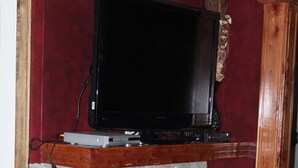 A stone fireplace with a television on top, a wooden mantel, and a red wall in the background. - Lazy G #1 Honeymoon Suite (Union Grove)