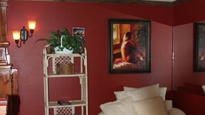 A living room with a white sofa, a wooden floor, a red wall, a white shelving unit, and a painting. - Lazy G #1 Honeymoon Suite (Union Grove)