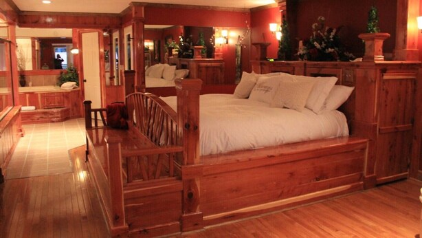 A cozy wooden bedroom with a large bed, a wooden bench, and a small table. - Lazy G #1 Honeymoon Suite (Union Grove)