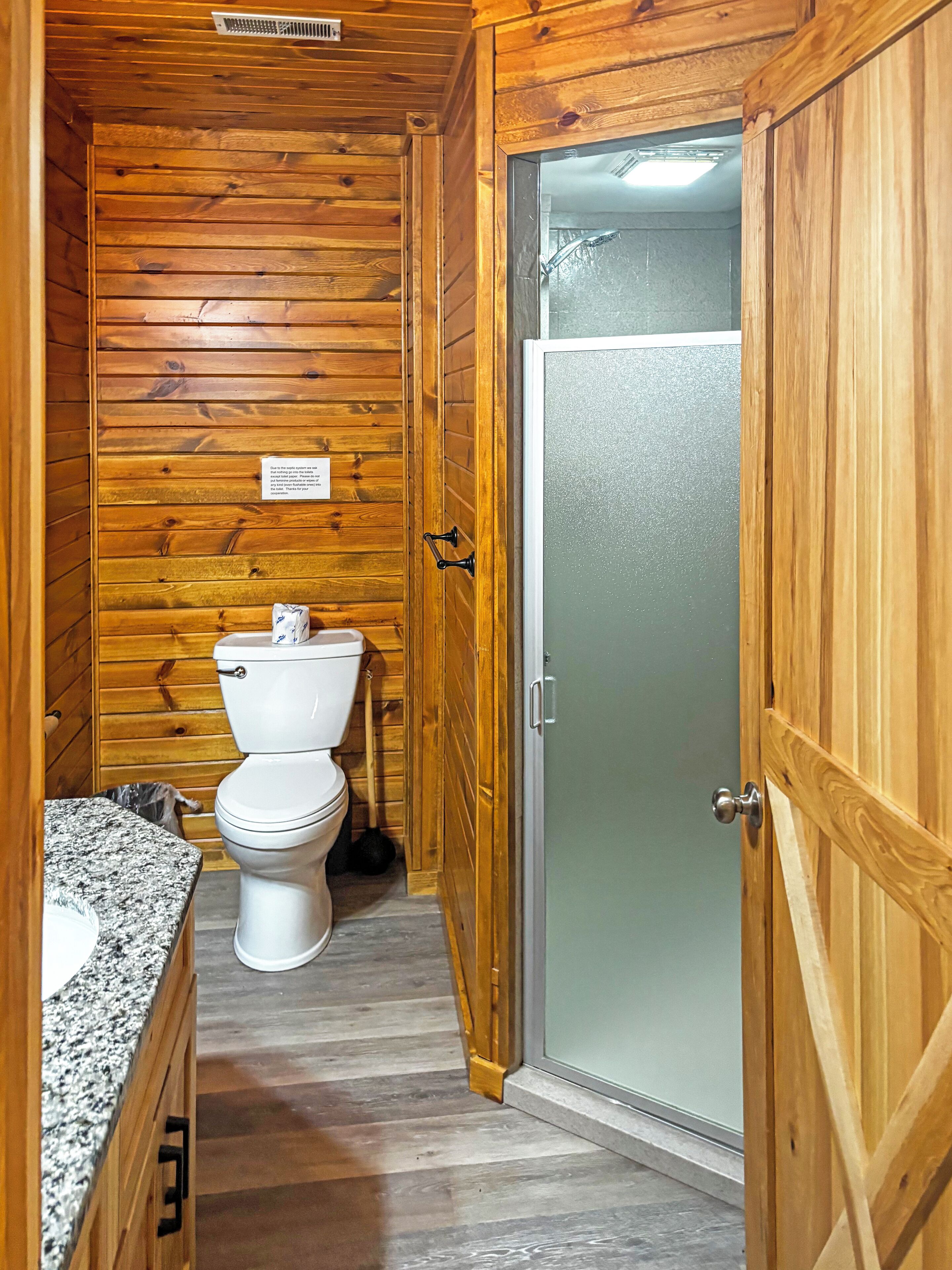 A wooden-paneled bathroom with a toilet, a sink, and a shower door.