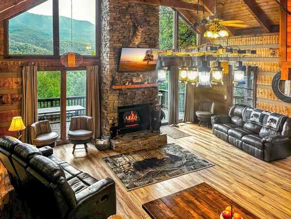 Un salón acogedor con chimenea de piedra, sofás de cuero y un ventanal con vistas a zona boscosa.