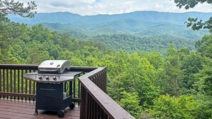 A deck with a grill overlooking a forested mountain range.