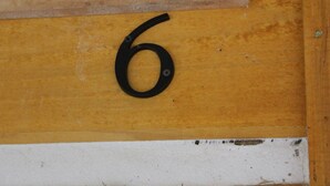 Un chiffre « 6 » en métal noir, fixé sur un mur jaune.