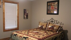 Une chambre à coucher avec un lit recouvert d’une courtepointe à motifs équestres, une fenêtre avec des stores et un mur orné d’une affiche sur le thème du rodéo.