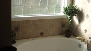 A bathroom with a large bathtub, a window with decorative glass, and a potted plant. - Lazy G Cabin #4 Creeks Edge (Union Grove)