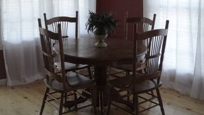 A dining area with a round wooden table surrounded by six wooden chairs. There is a potted plant on the table. The room has red walls and white curtains on the windows. - Lazy G Cabin #4 Creeks Edge (Union Grove)