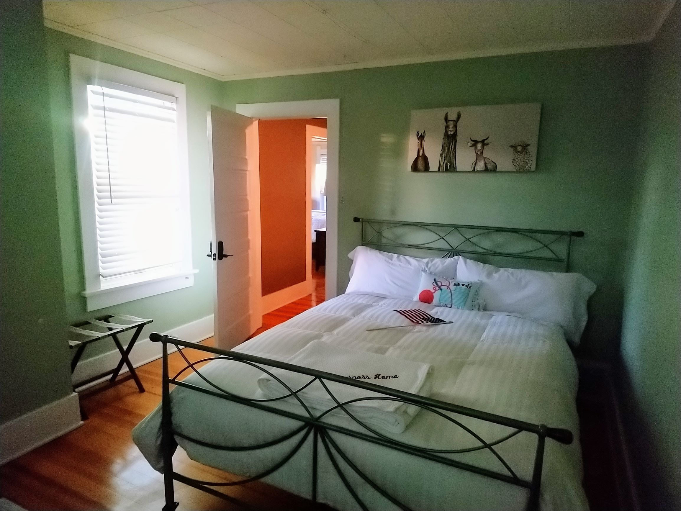Ein Schlafzimmer mit einem Metallbettgestell, weißer Bettwäsche und einem Gemälde an der Wand.