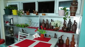 Uma área de refeições com uma mesa posta para dois, rodeada por estantes com diversos objetos de cerâmica e plantas.
