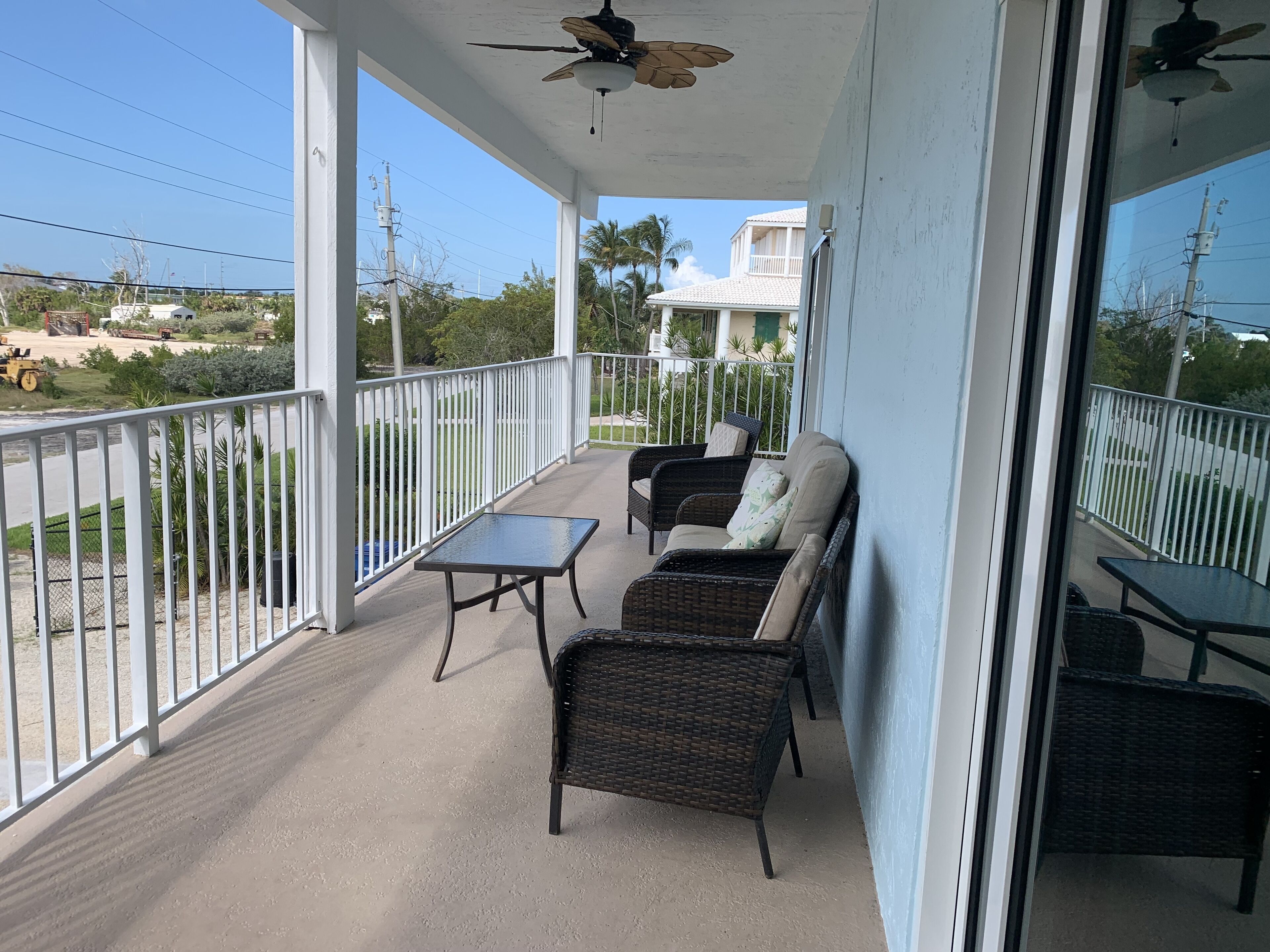 A covered balcony with wicker furniture, a table, and a ceiling fan.