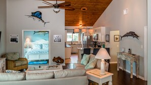 A spacious living room with a high ceiling, a ceiling fan, a sofa, a coffee table, and a dining area with a kitchen in the background. - FALL SEASON 55% OFF RENTAL RATE (Marathon)