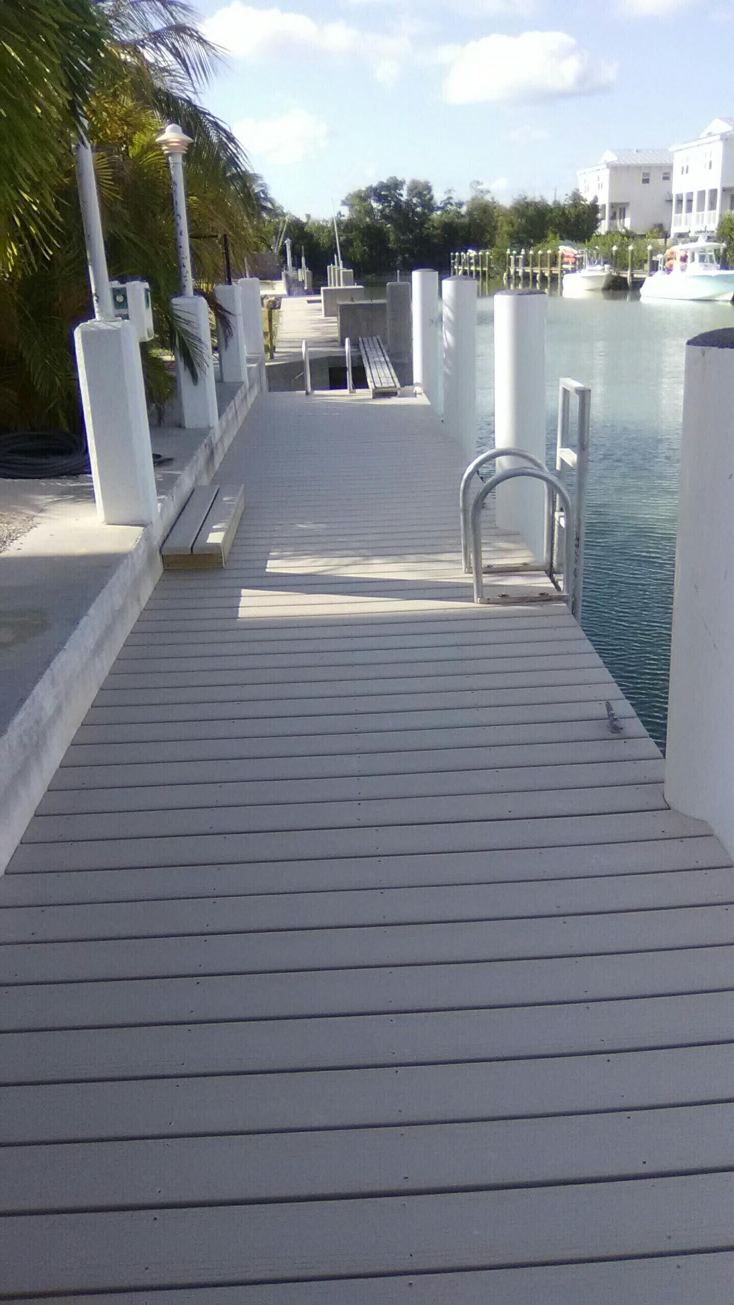 A wooden dock leading to a body of water with a bench and lamp posts along the side.