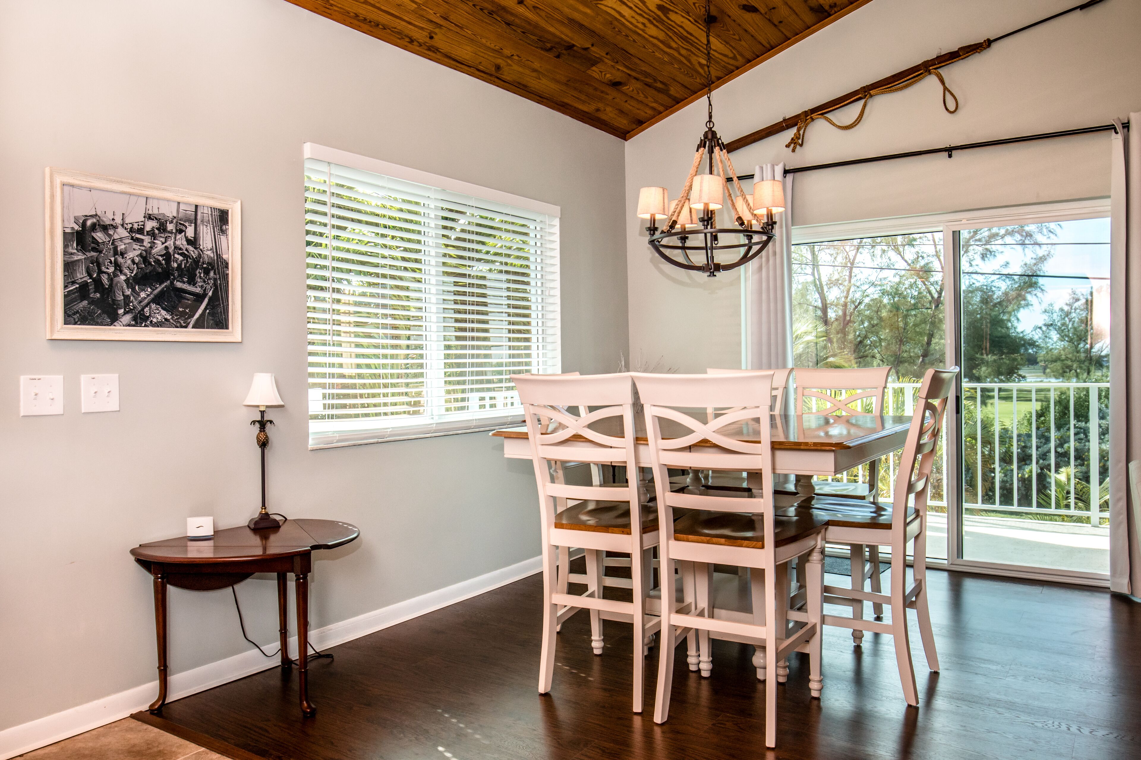 A dining area with a wooden table and chairs, a chandelier, a framed historical photo, and a window with blinds.