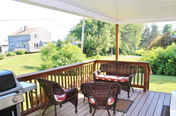 A covered porch with wicker chairs and a grill.
