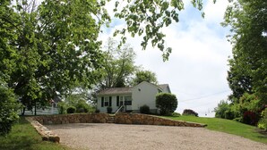 A house with a stone retaining wall, a gravel driveway, and a lawn.
