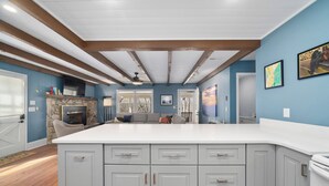 A modern kitchen with grey cabinets, a white countertop, and a stone fireplace.