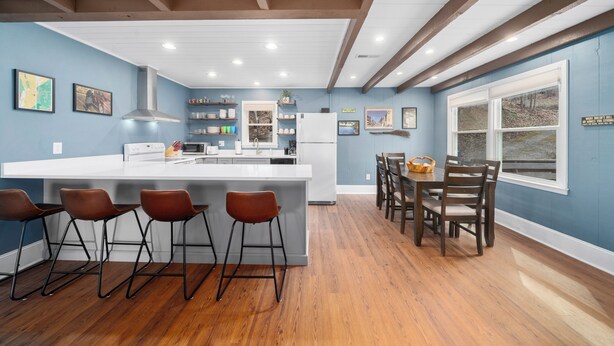 A modern kitchen with a central island, bar stools, wooden dining table, and chairs.
