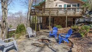 A stone patio with a fire pit, two blue Adirondack chairs, and a white chair.