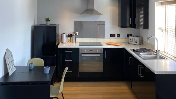 Una cocina moderna con tragaluz, armarios negros, un comedor con mesa y sillas, e iluminación colgante.