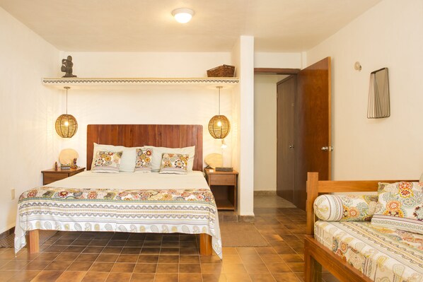 A bedroom with a wooden bed, two bedside tables with lamps, a patterned bedspread, and a door leading to another room.