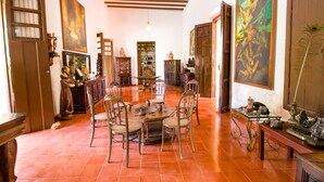 Amplia habitación con suelo de baldosas, una mesa redonda de madera con sillas y una estantería llena de libros y objetos decorativos.