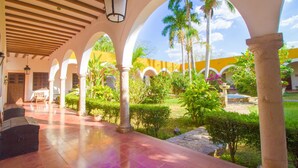 Un espacio al aire libre techado con arcos, columnas y un jardín con palmeras y arbustos.