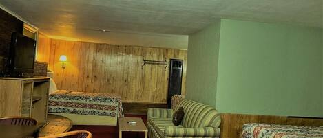 A room with a bed, a sofa, a small table, a TV, and a lamp.
