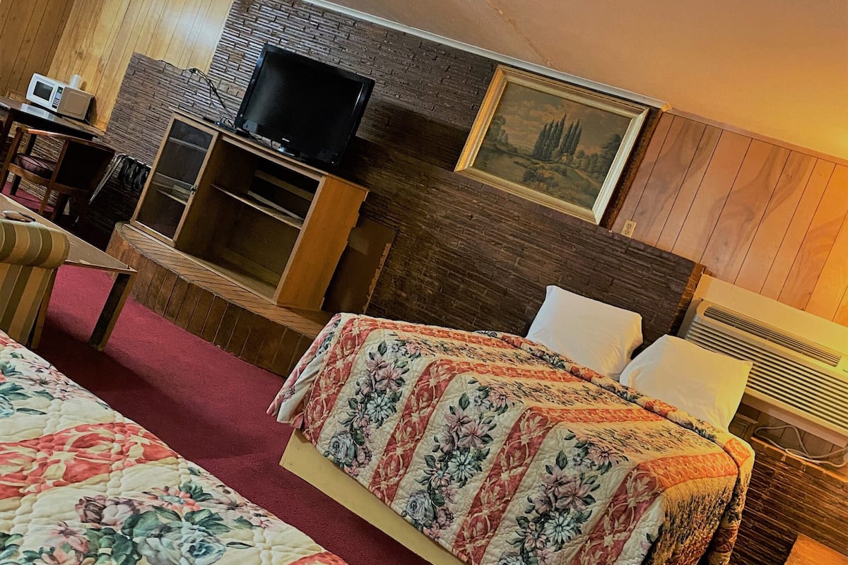 A hotel room with two beds, a TV, a desk, and a painting on the wall.