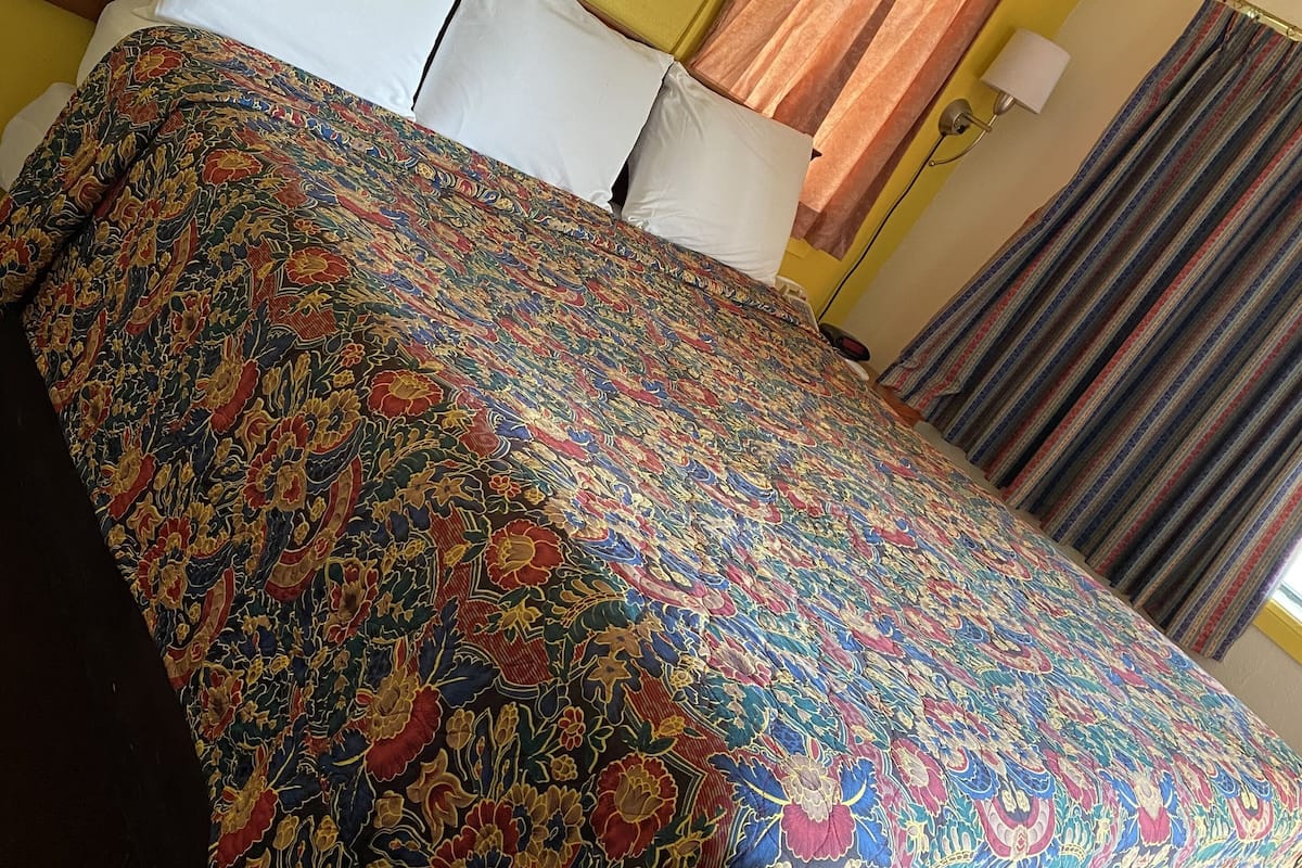 A hotel room with a bed, a nightstand, a lamp, and a painting on the wall.
