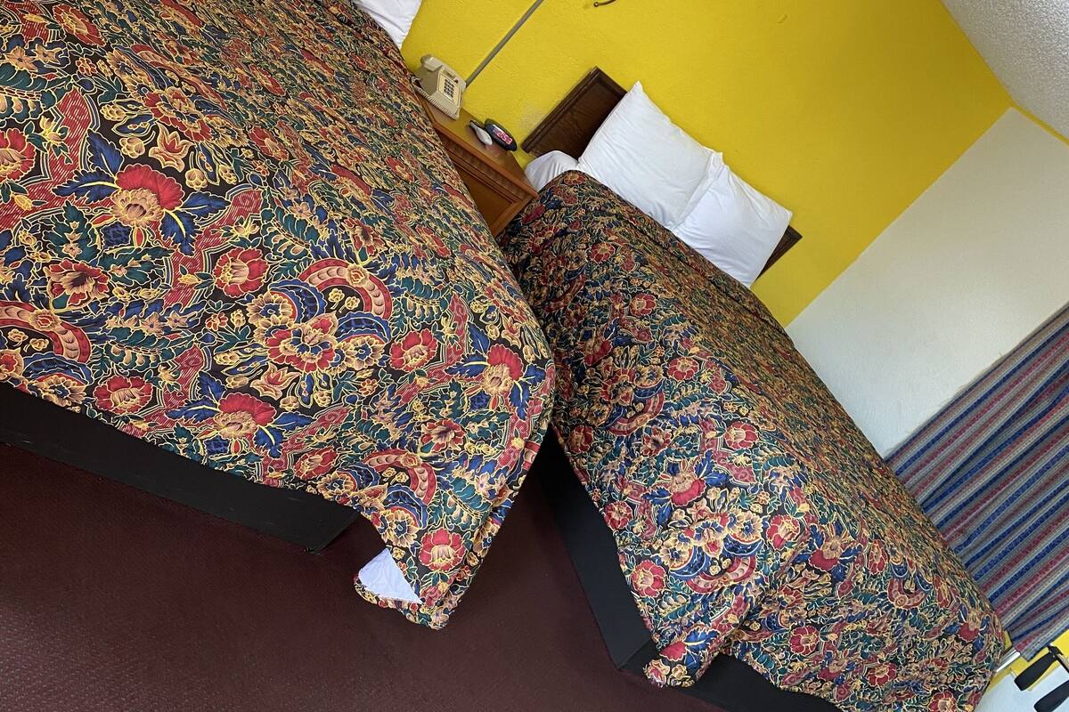 A hotel room with two beds, a nightstand, a lamp, and a telephone.